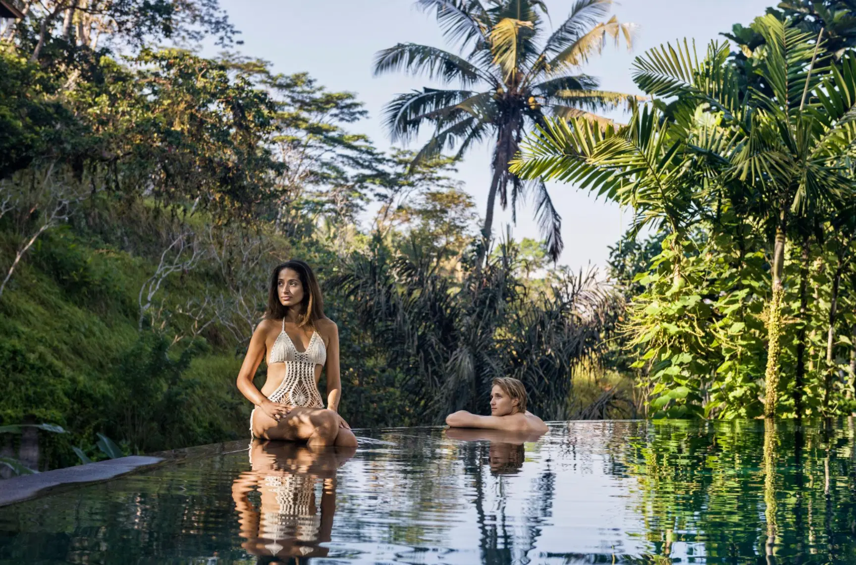 A woman and man relaxing in an infinity pool surrounded by tropical palms